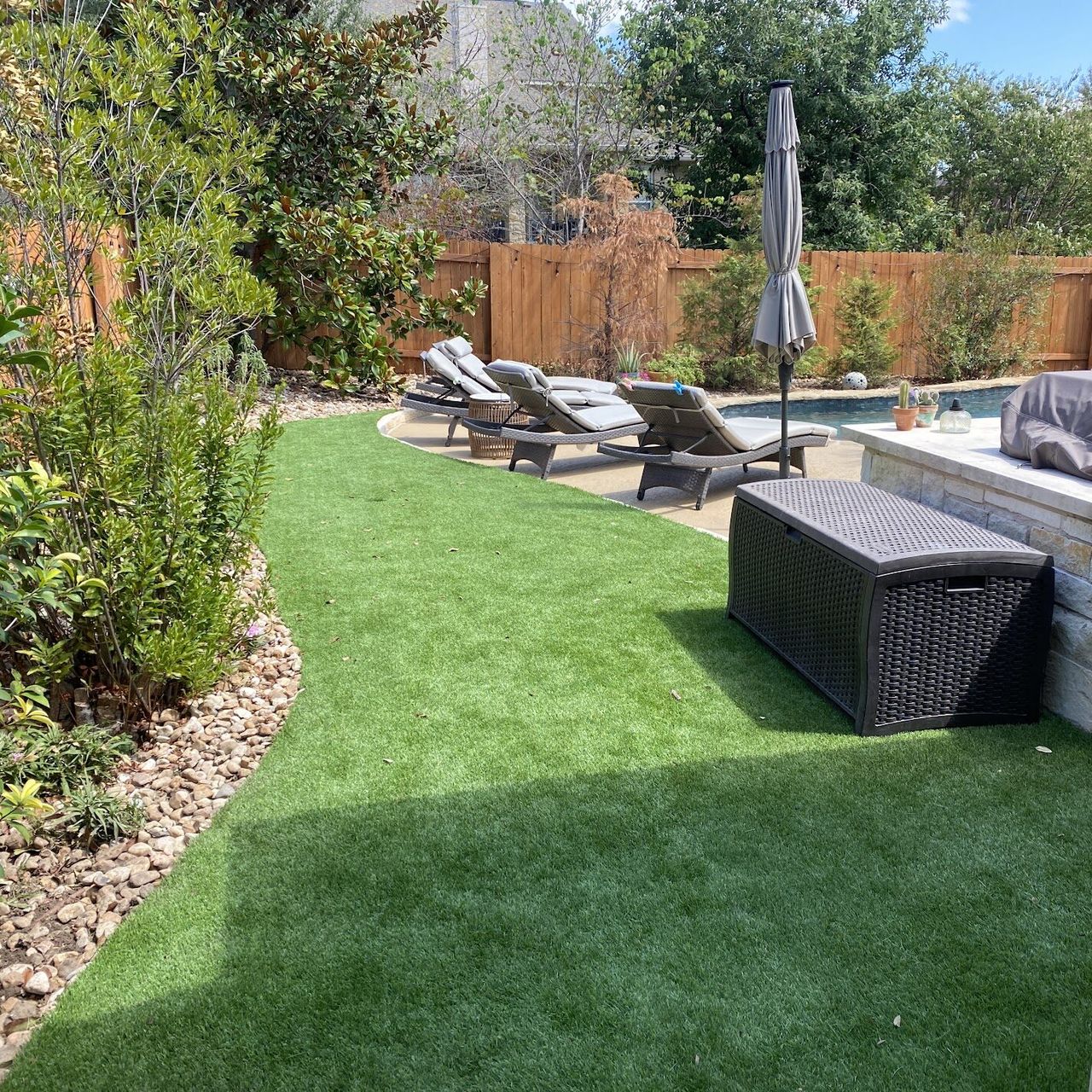 Curved artificial turf area with a river rock border beside a pool in an Austin backyard