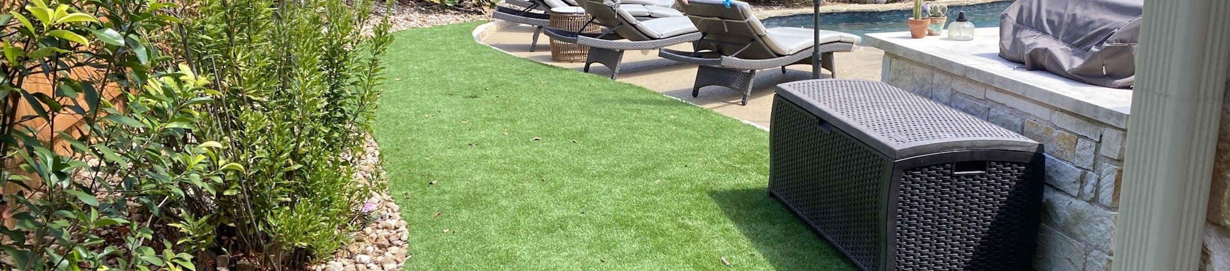 Artificial turf lawn curving along a river rock border and planting bed beside a backyard pool in Austin