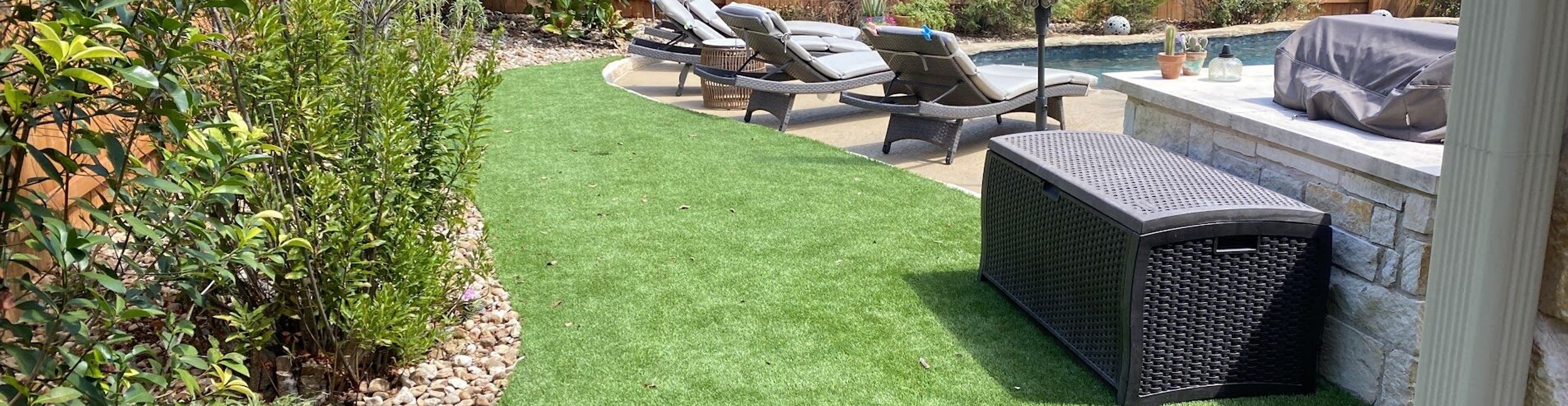 Artificial turf lawn curving along a river rock border and planting bed beside a backyard pool in Austin