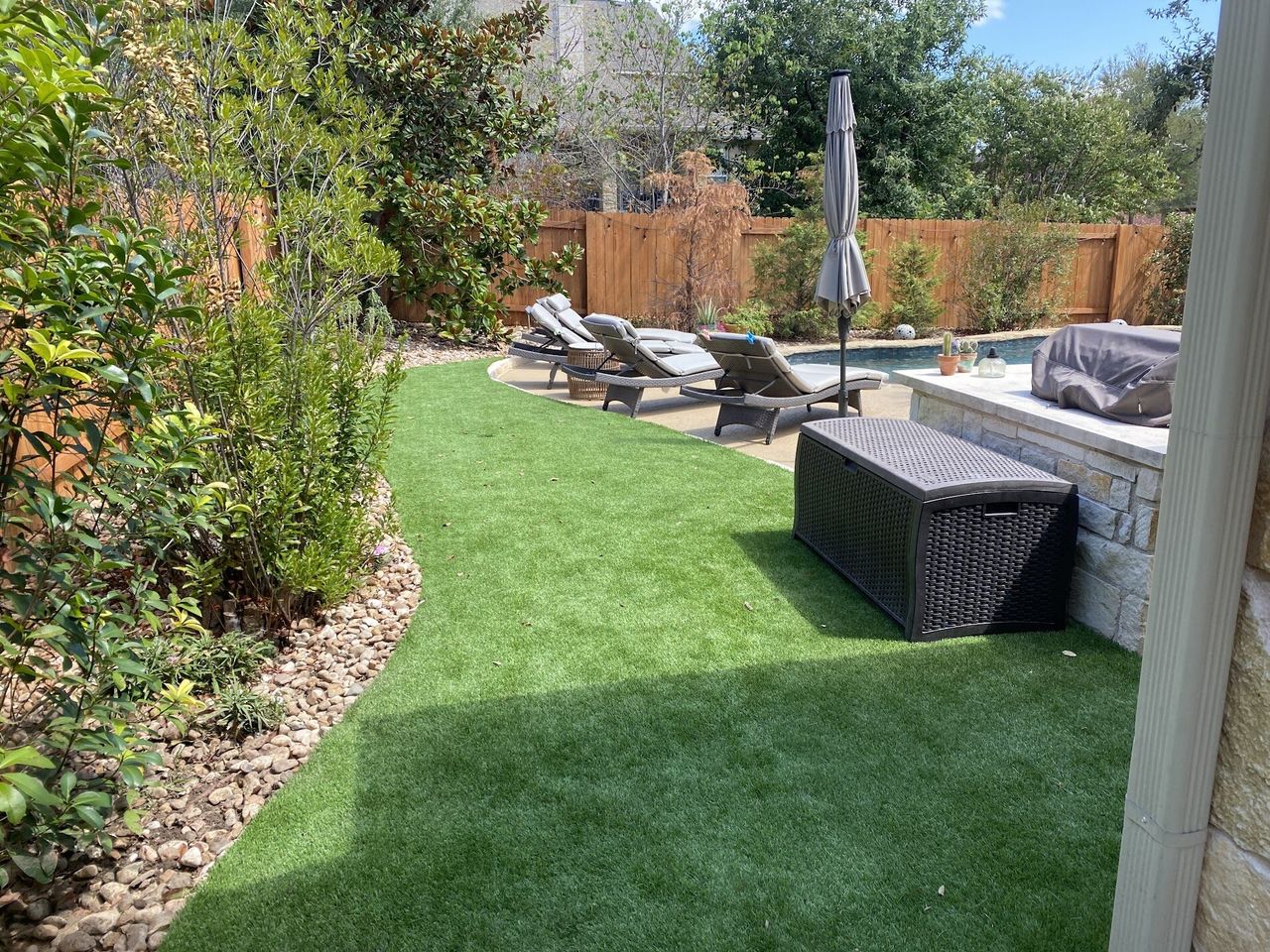 Artificial turf lawn with a river rock border curving beside a backyard pool in Austin