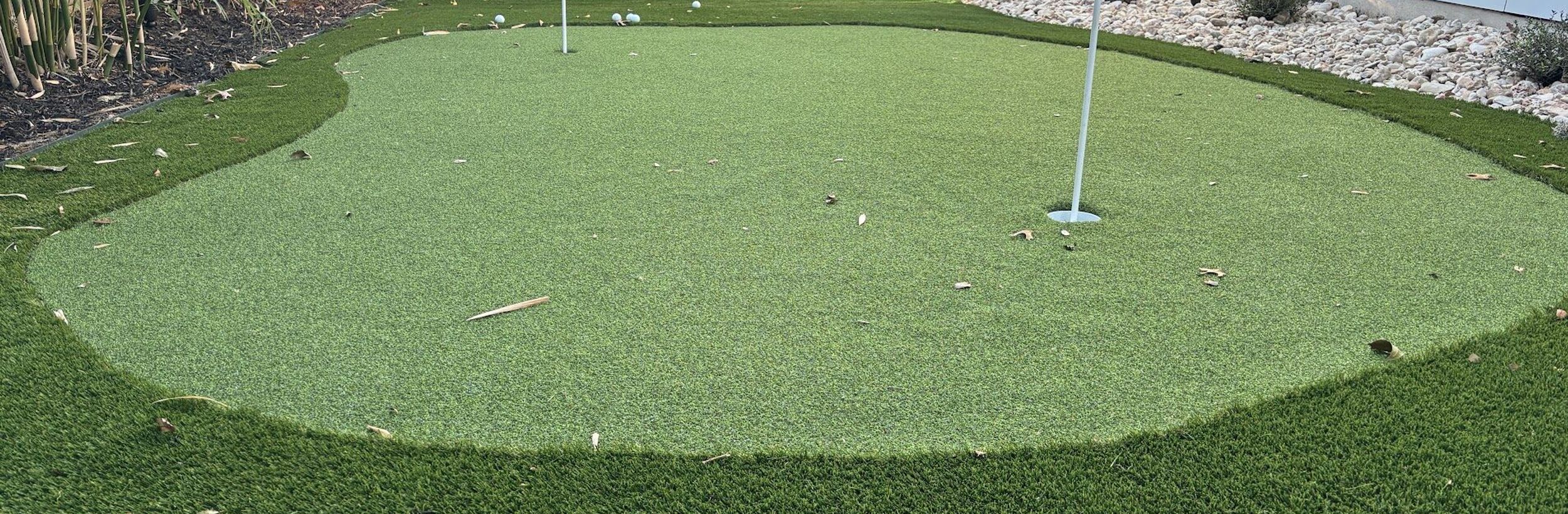 Backyard artificial turf putting green with two flags, a river rock border, and a cedar privacy fence in Austin