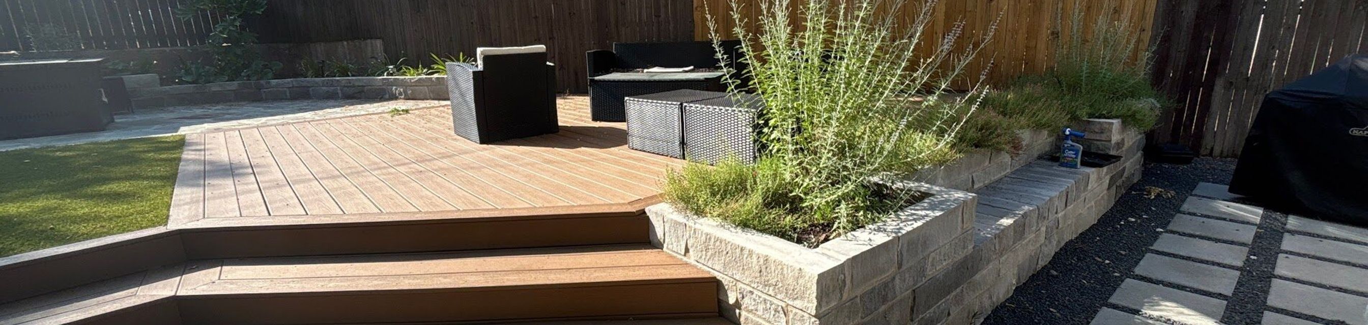 Composite deck with wide wraparound steps and a limestone block planter built by GardenGOAT in Austin