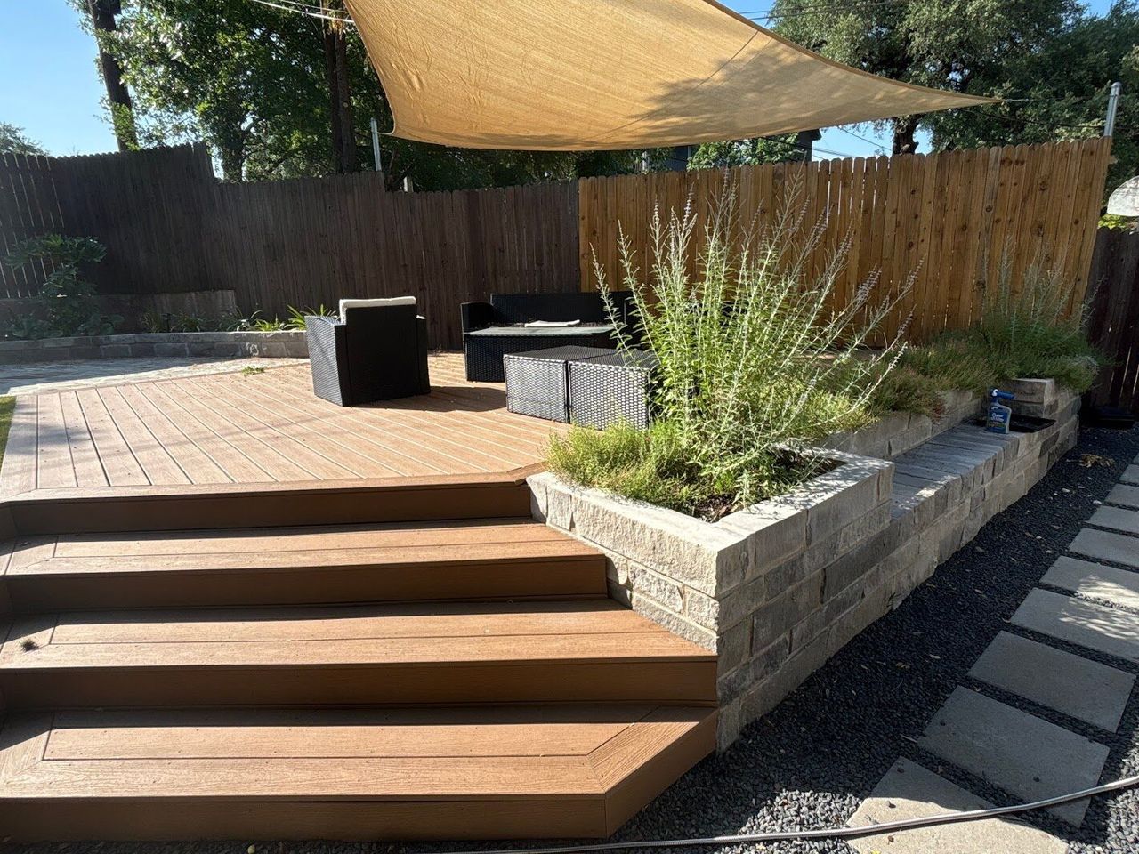 Raised limestone block planter bed built alongside a composite deck in an Austin backyard