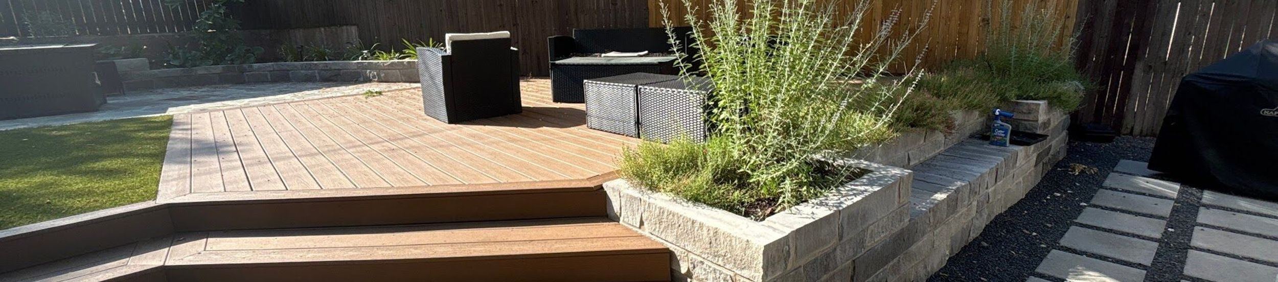 Composite deck with wide wraparound steps, a limestone block planter, and concrete pavers set in black gravel in an Austin backyard