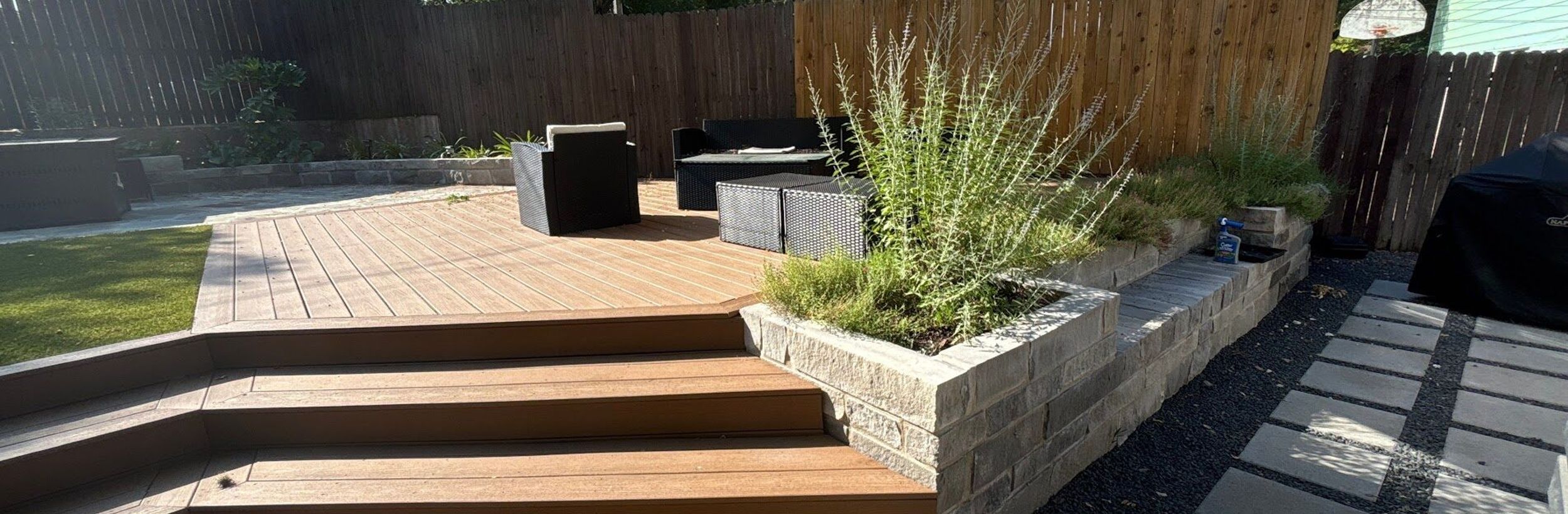 Composite deck with wide wraparound steps, a limestone block planter, and concrete pavers set in black gravel in an Austin backyard