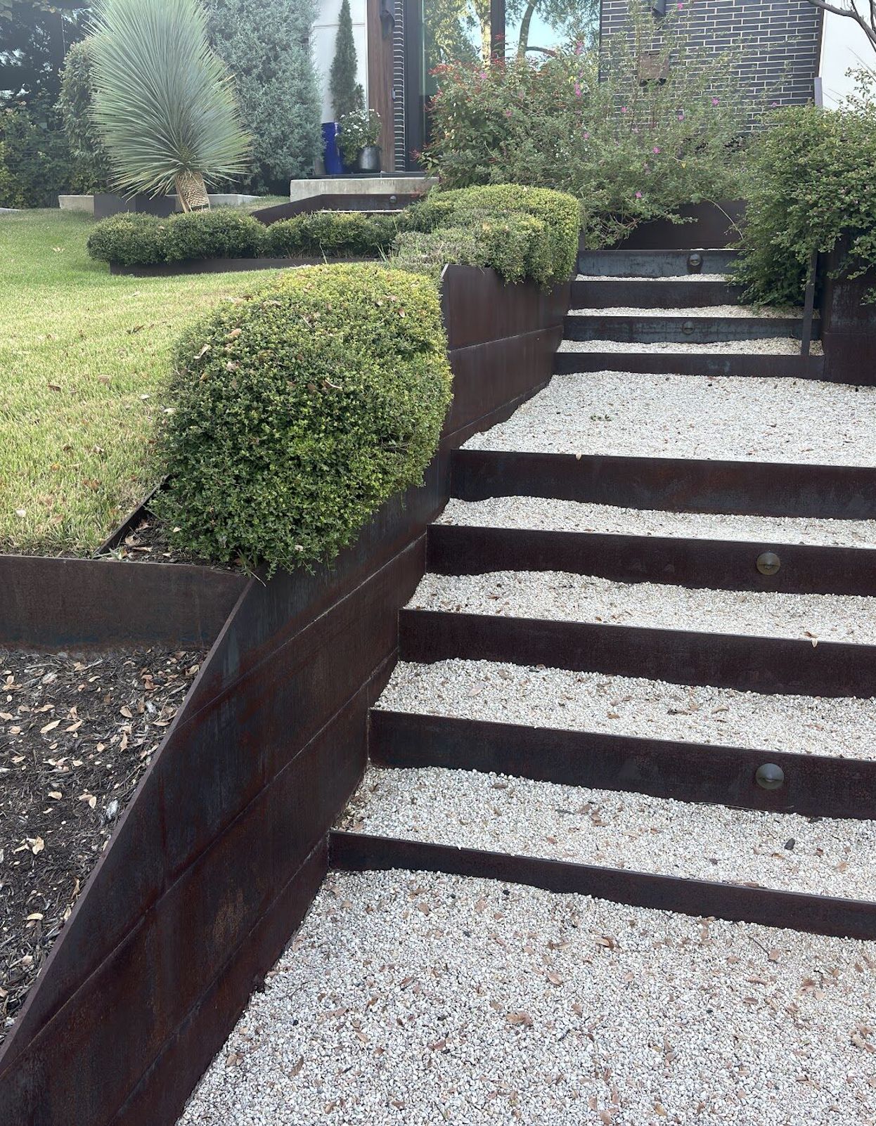 Corten steel steps filled with gravel between terraced steel-edged planting beds in an Austin landscape by GardenGOAT