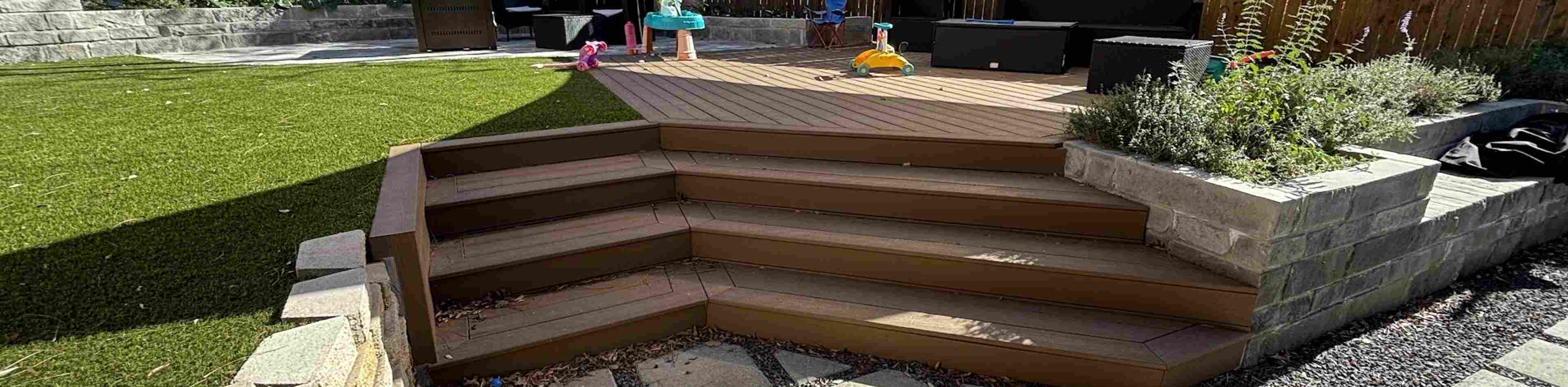 Austin backyard transformation with artificial turf, a composite deck with wraparound steps, a stone block planter, and concrete pavers in gravel