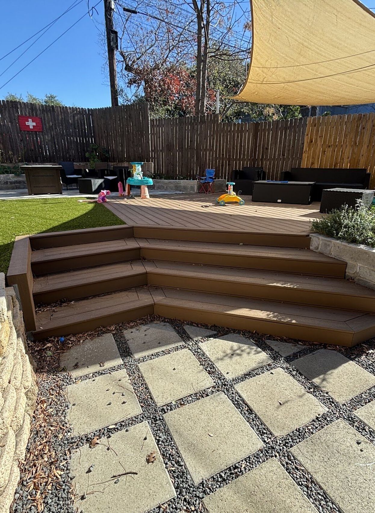 Austin backyard transformation by GardenGOAT with artificial turf, a composite deck with wraparound steps, a stone block planter, and concrete pavers in gravel