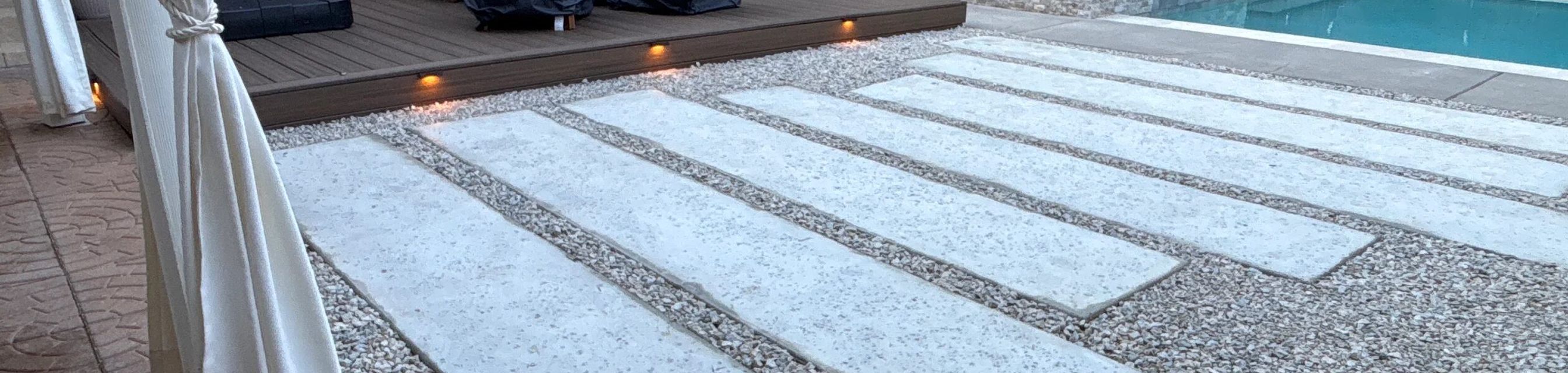 Backyard landscape design in Austin with a lit composite deck, large concrete pavers in gravel, and a pool and spa