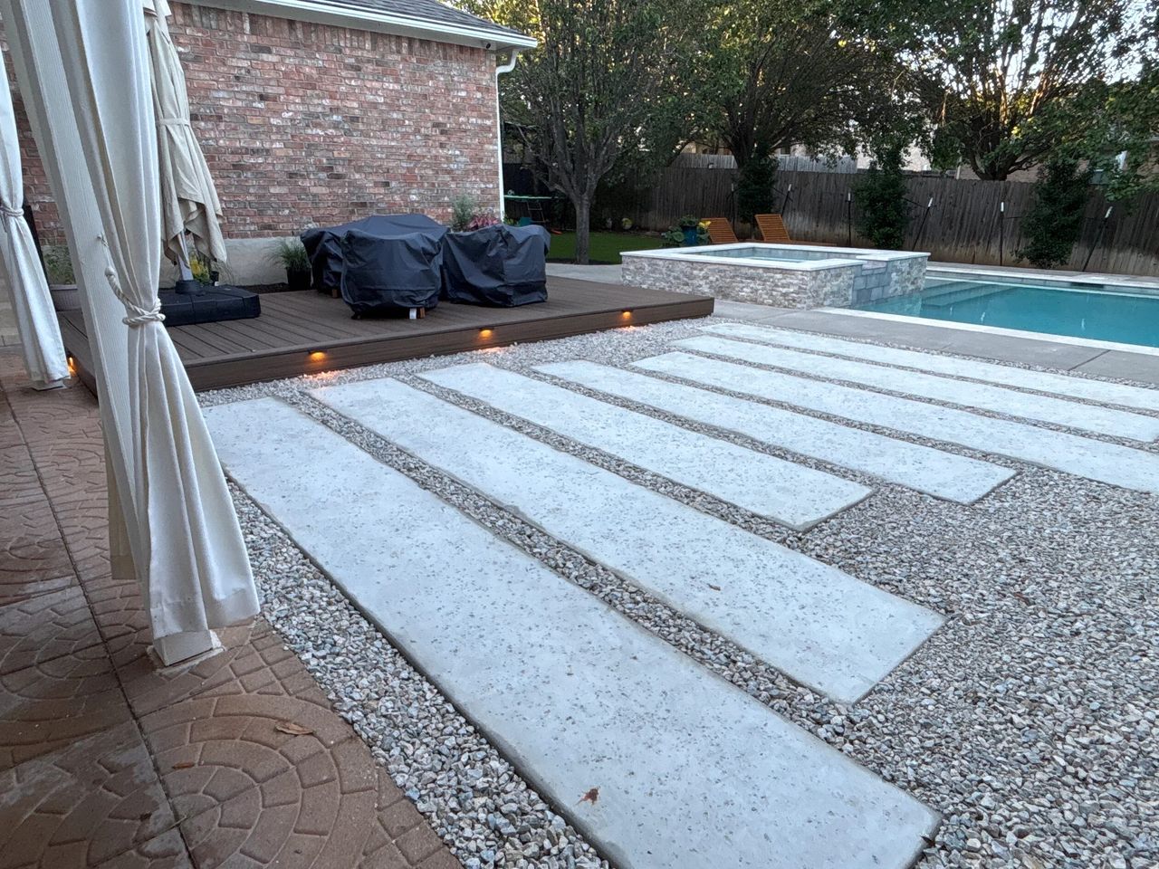 Hardscape design with large concrete pavers in gravel, a lit composite deck, and a pool in Austin