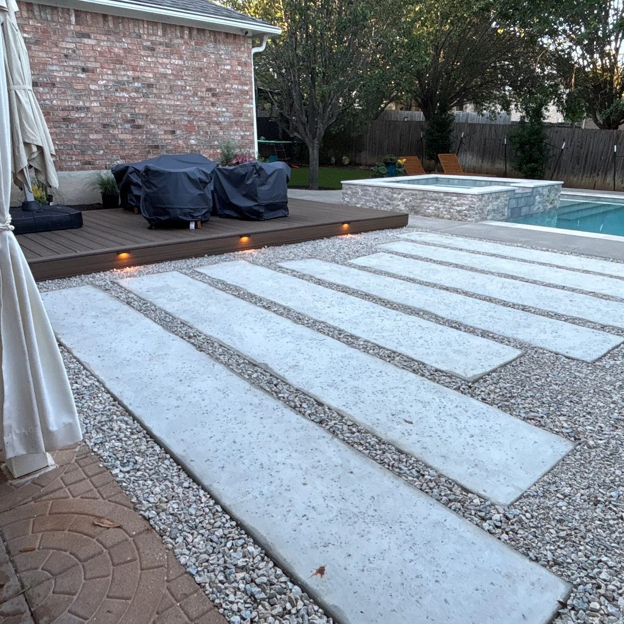 Composite deck with built-in step lights beside a pool and spa in an Austin backyard