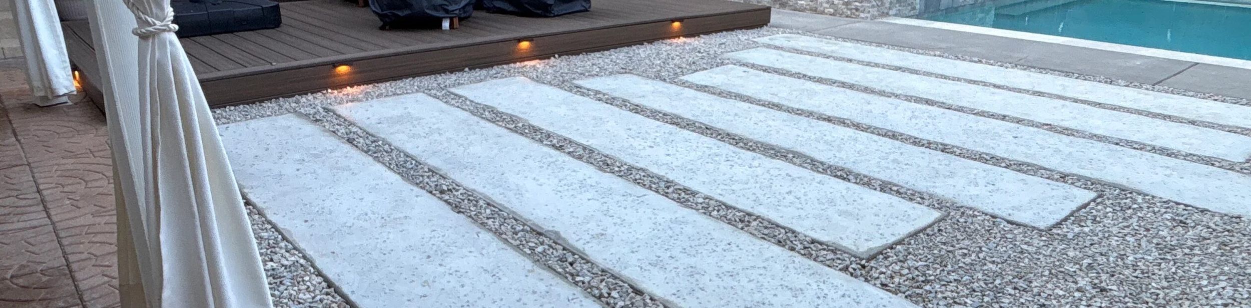 Backyard with a lit composite deck, large concrete pavers set in gravel, and a pool and spa in Austin