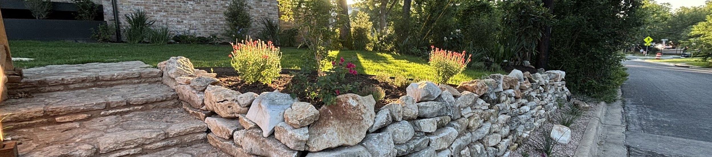 Dry-stacked limestone retaining wall and natural stone steps in a front yard landscape in Austin