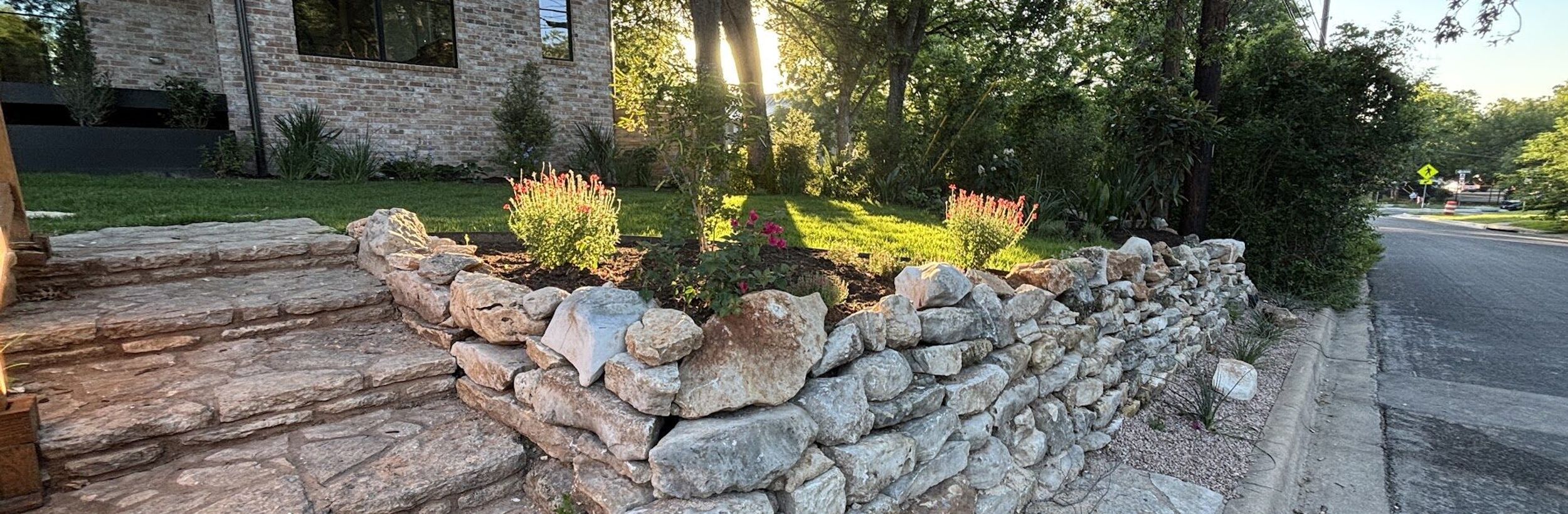 Dry-stacked limestone retaining wall and natural stone steps in a front yard landscape in Austin