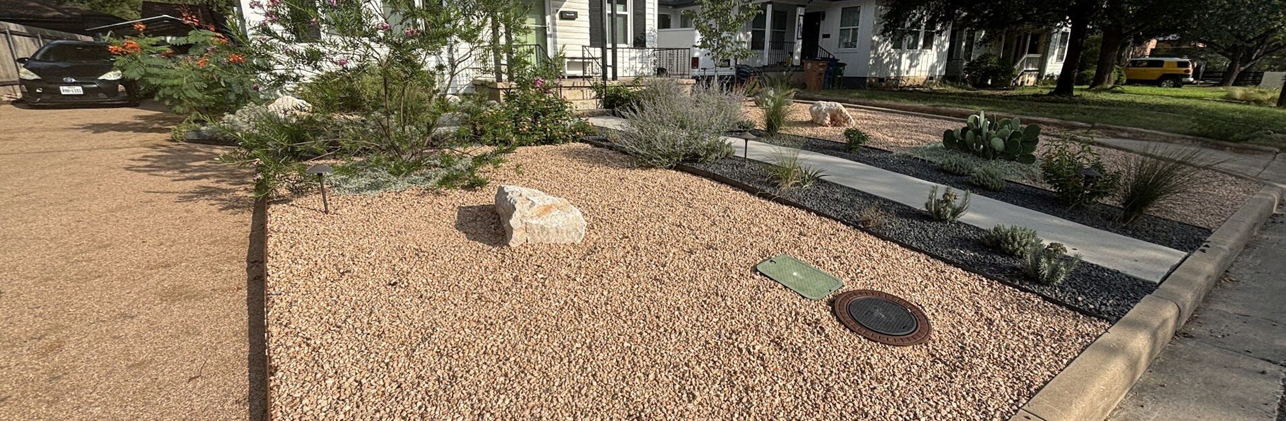 Front yard xeriscape with crushed granite, a boulder accent, native plants, and a concrete walkway in Austin