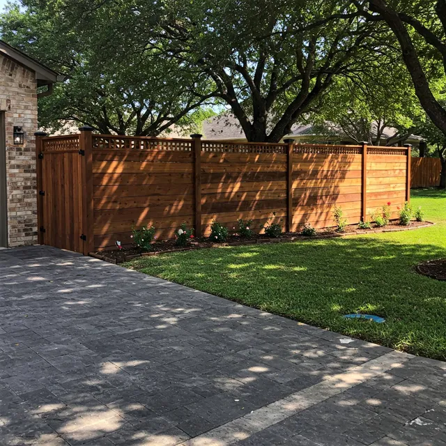 Stained horizontal cedar privacy fence with a lattice top and matching gate beside a paver driveway, shaded by mature live oaks