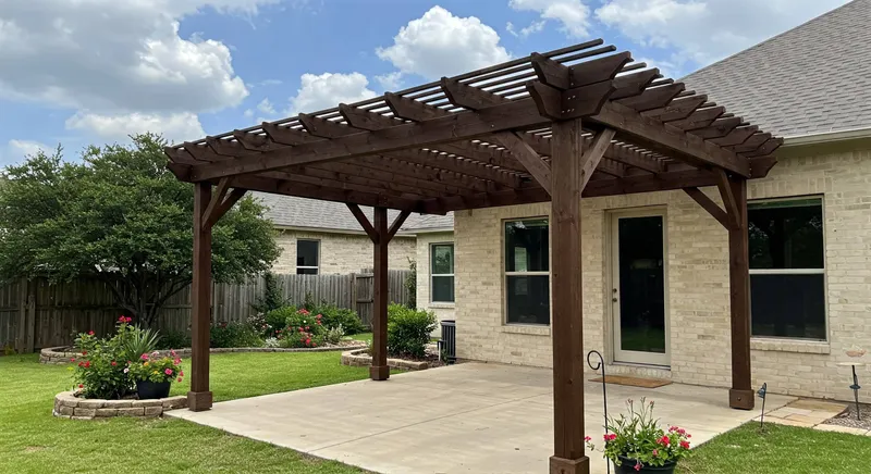 Wood pergola over a concrete patio beside a brick home and raised garden beds