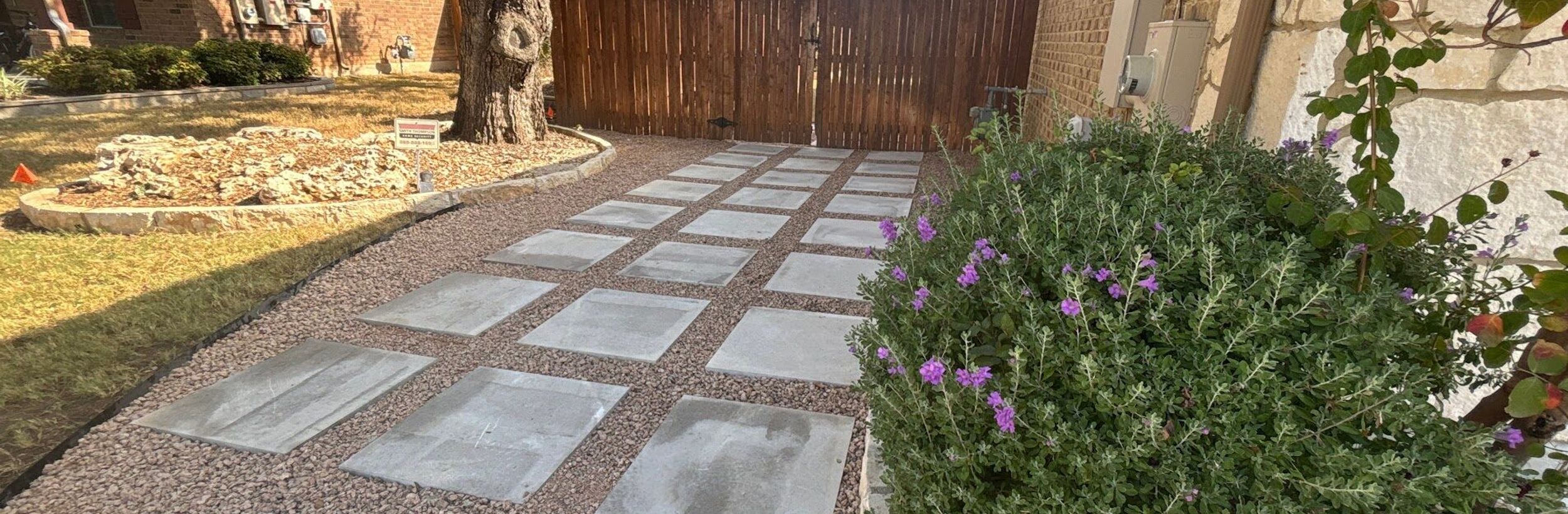 Large concrete pavers set in crushed granite forming a side-yard pathway to a cedar gate in Austin