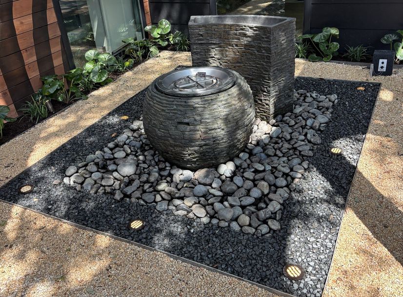 Stacked slate sphere fountain set in black river pebbles in Austin