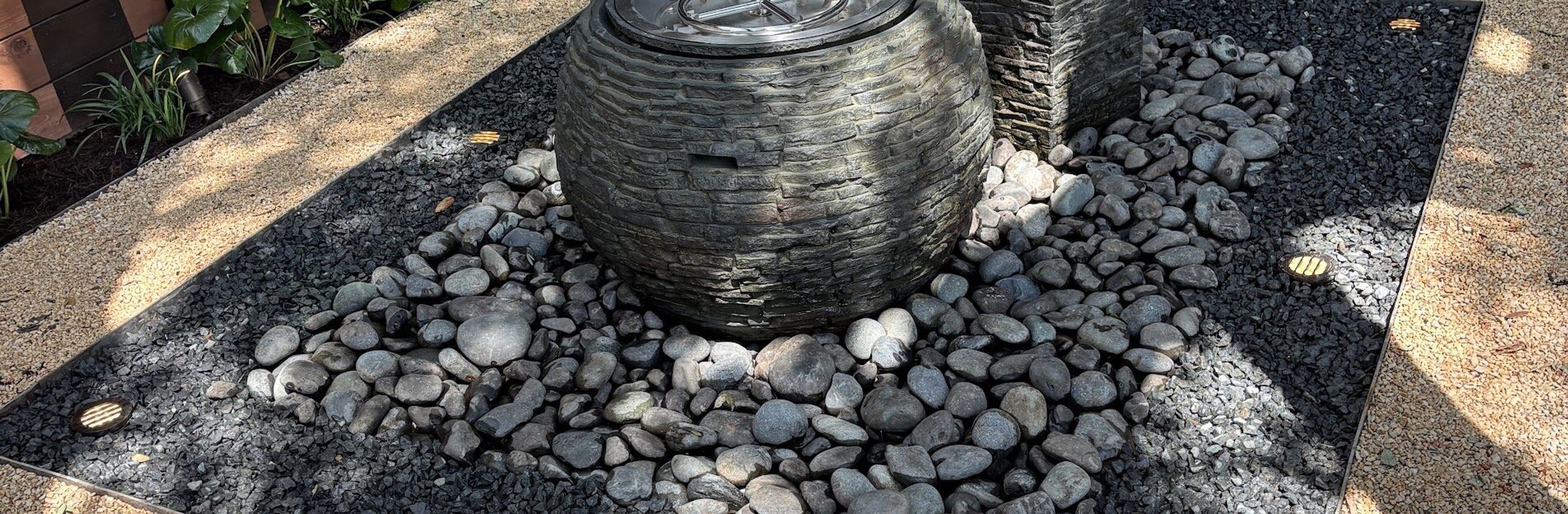 Stacked slate sphere fountain and column water feature set in black river pebbles with in-ground lights in Austin